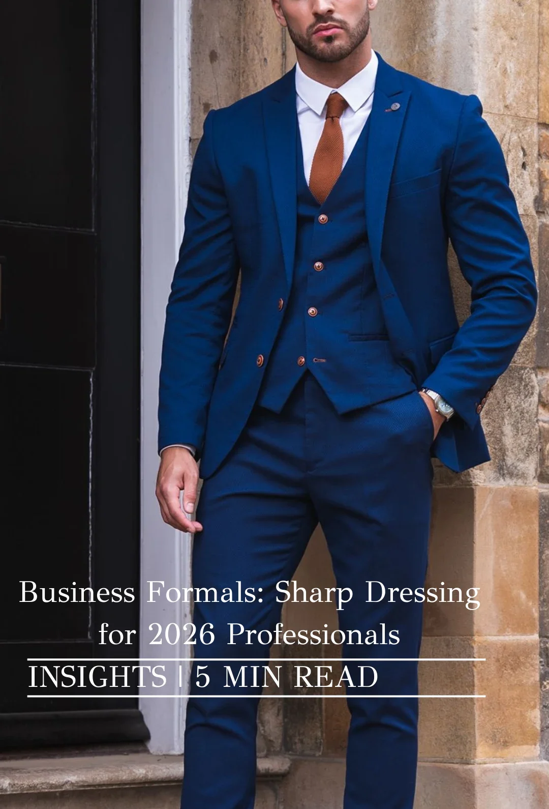 Man in deep navy three‑piece business formals with white shirt, brown tie, and tan Oxford shoes standing by a stone doorway—business formal outfit.